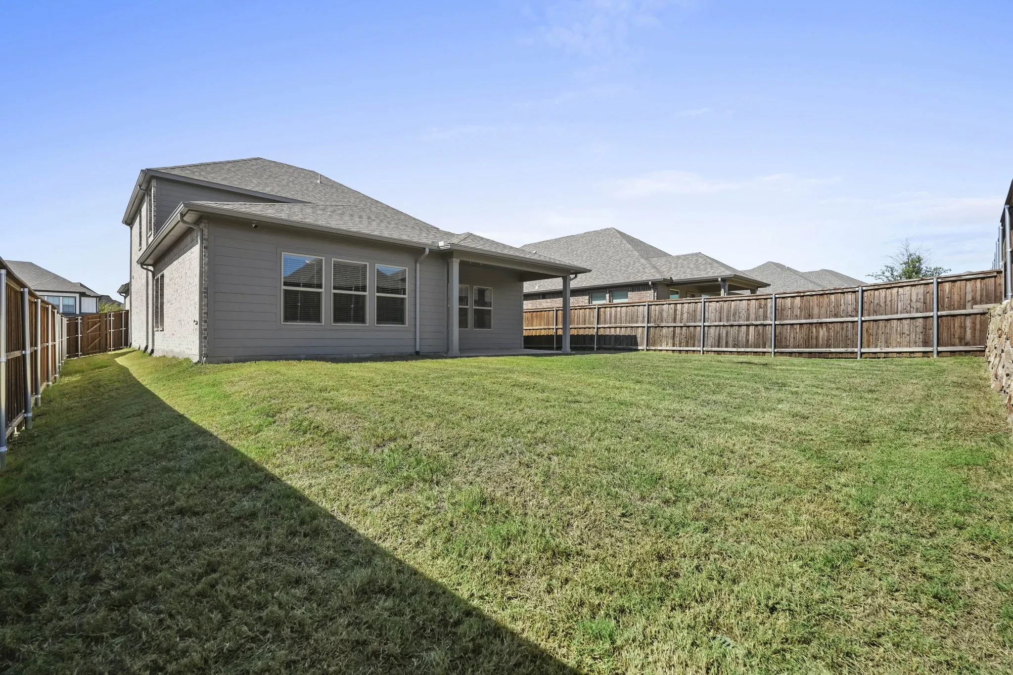 Expansive backyard with a flat lawn, wood-panel fencing, and a covered patio area
