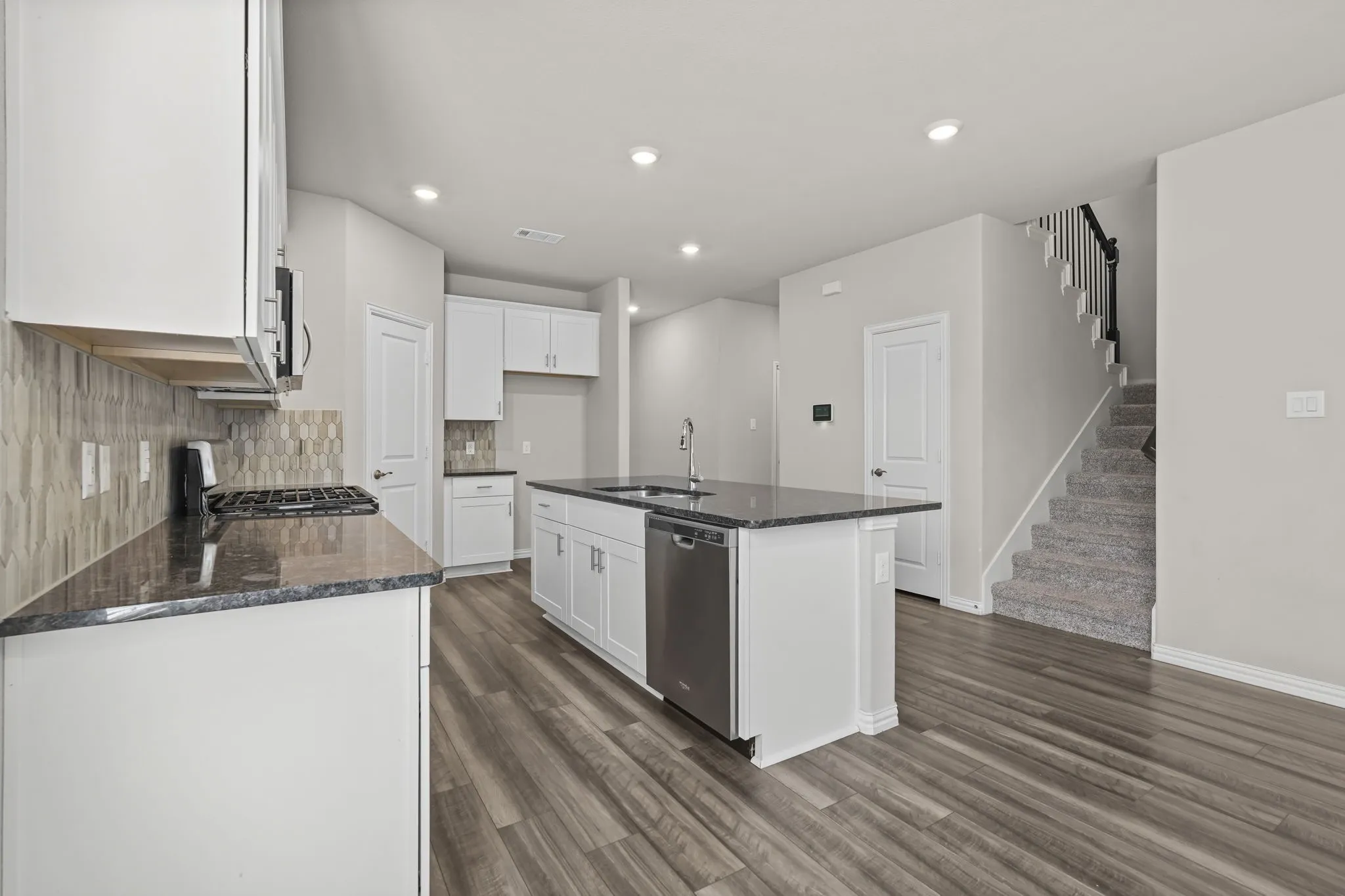 Open-concept kitchen with white cabinetry, dark granite countertops, and a full-height tiled backsplash