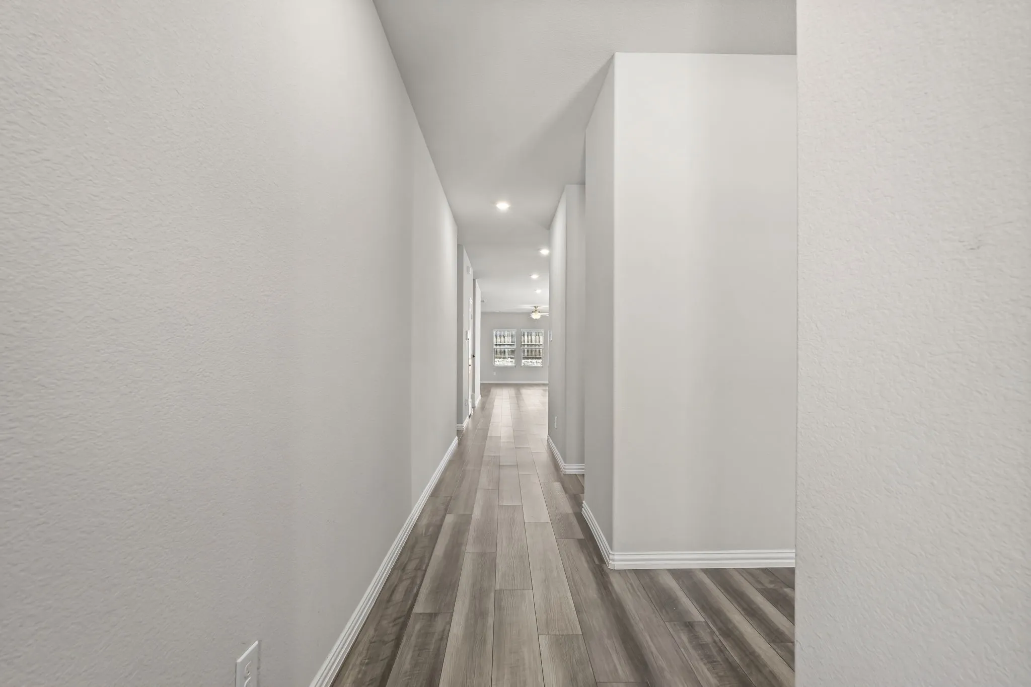 Recessed lighting illuminating a long hallway with wood-finish flooring and light-toned walls