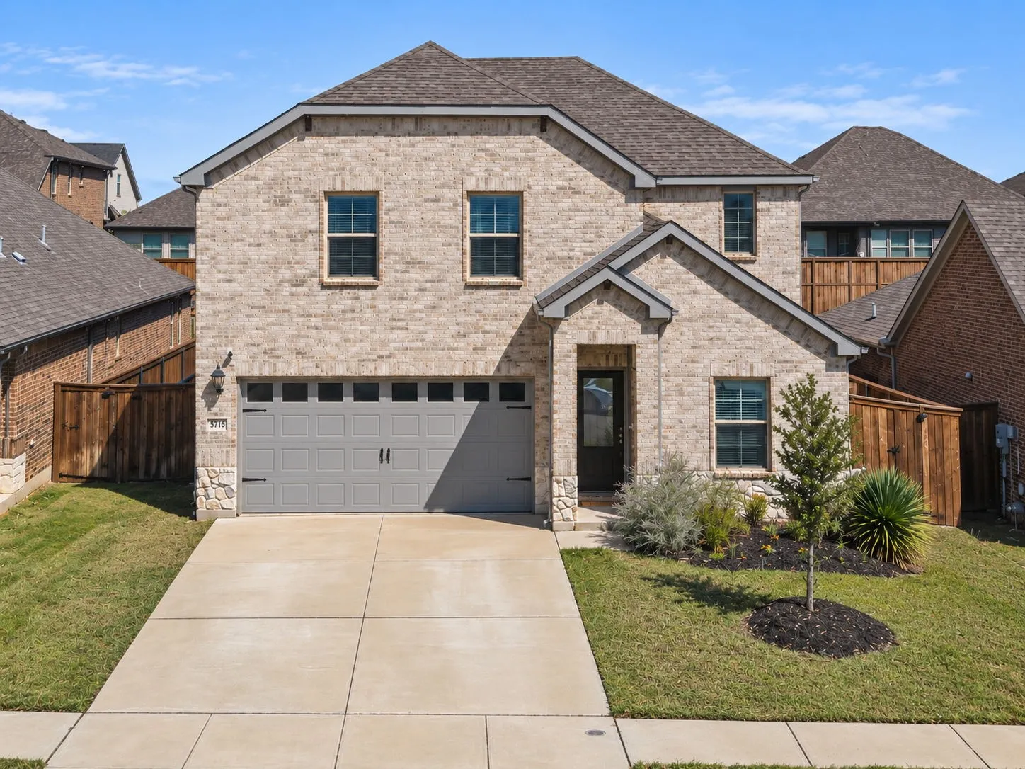 Brick exterior with stone accents, attached two-car garage, concrete driveway, front entry door, and landscaped front yard