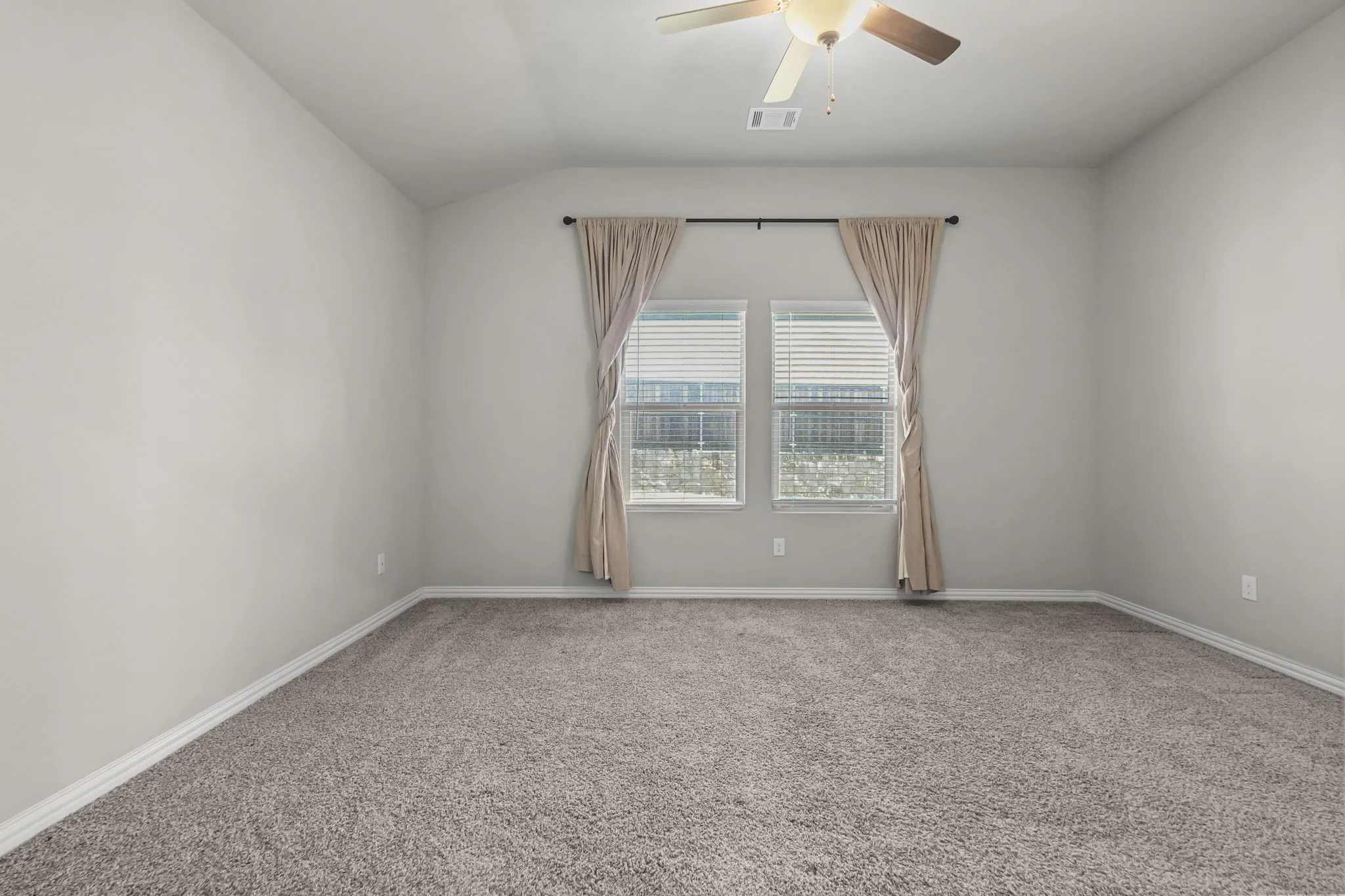 Recessed ceiling with a central ceiling fan, two windows with blinds, and neutral carpeting