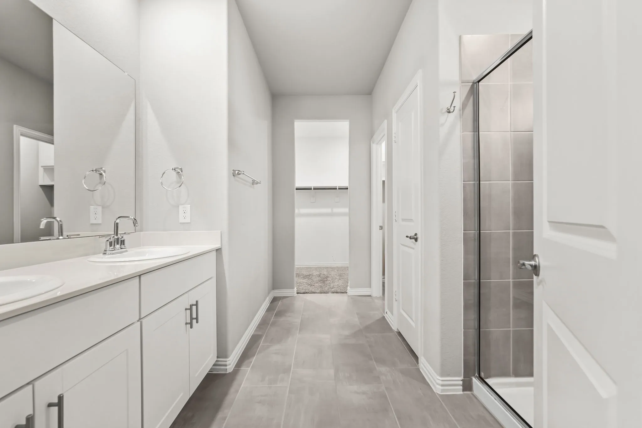 Dual vanity with white cabinetry and chrome fixtures, light-toned flooring, and a glass-enclosed shower with tiled walls