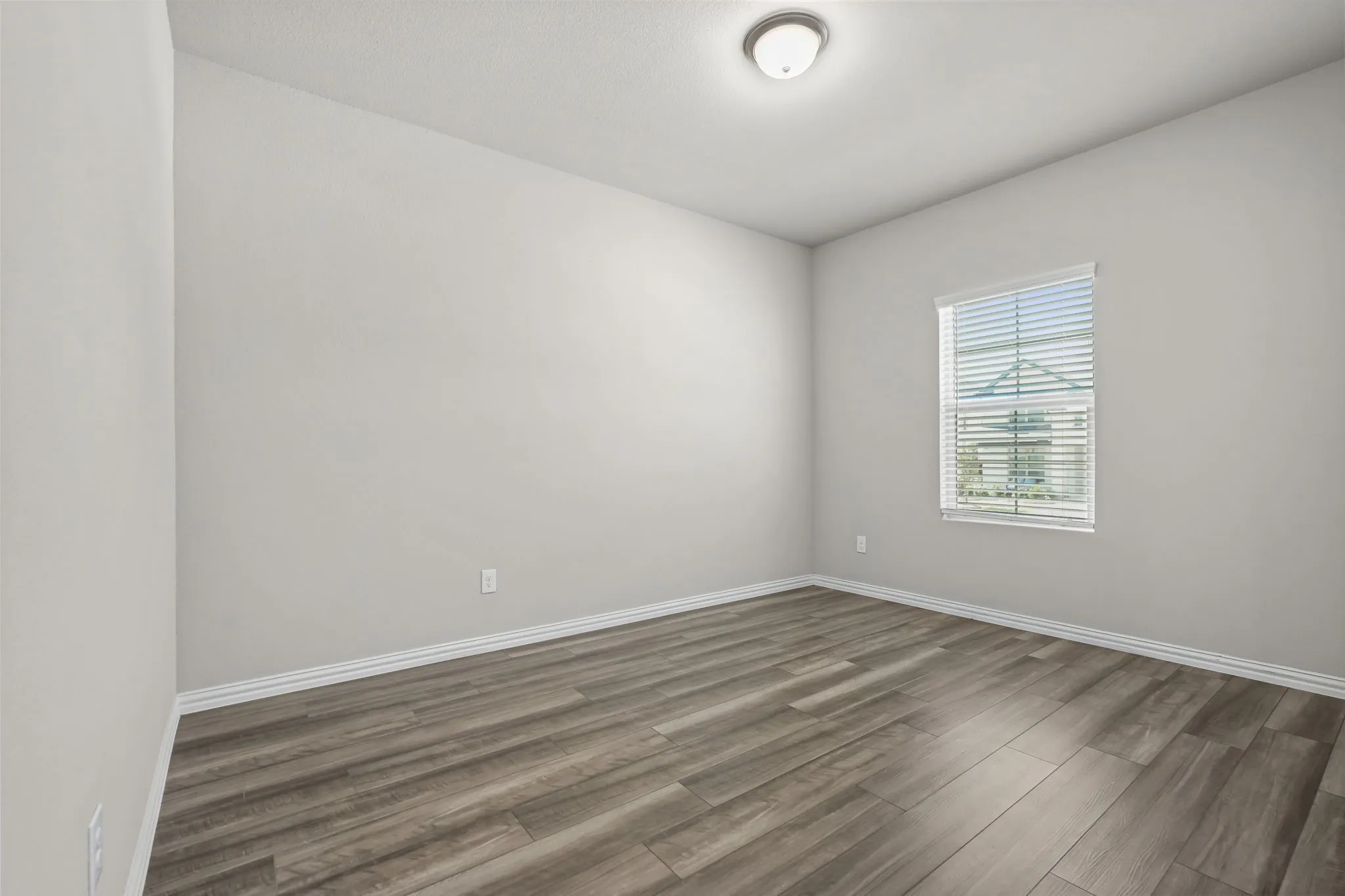 Wood-finish flooring, neutral wall tones, window with horizontal blinds, and a flush-mount ceiling light