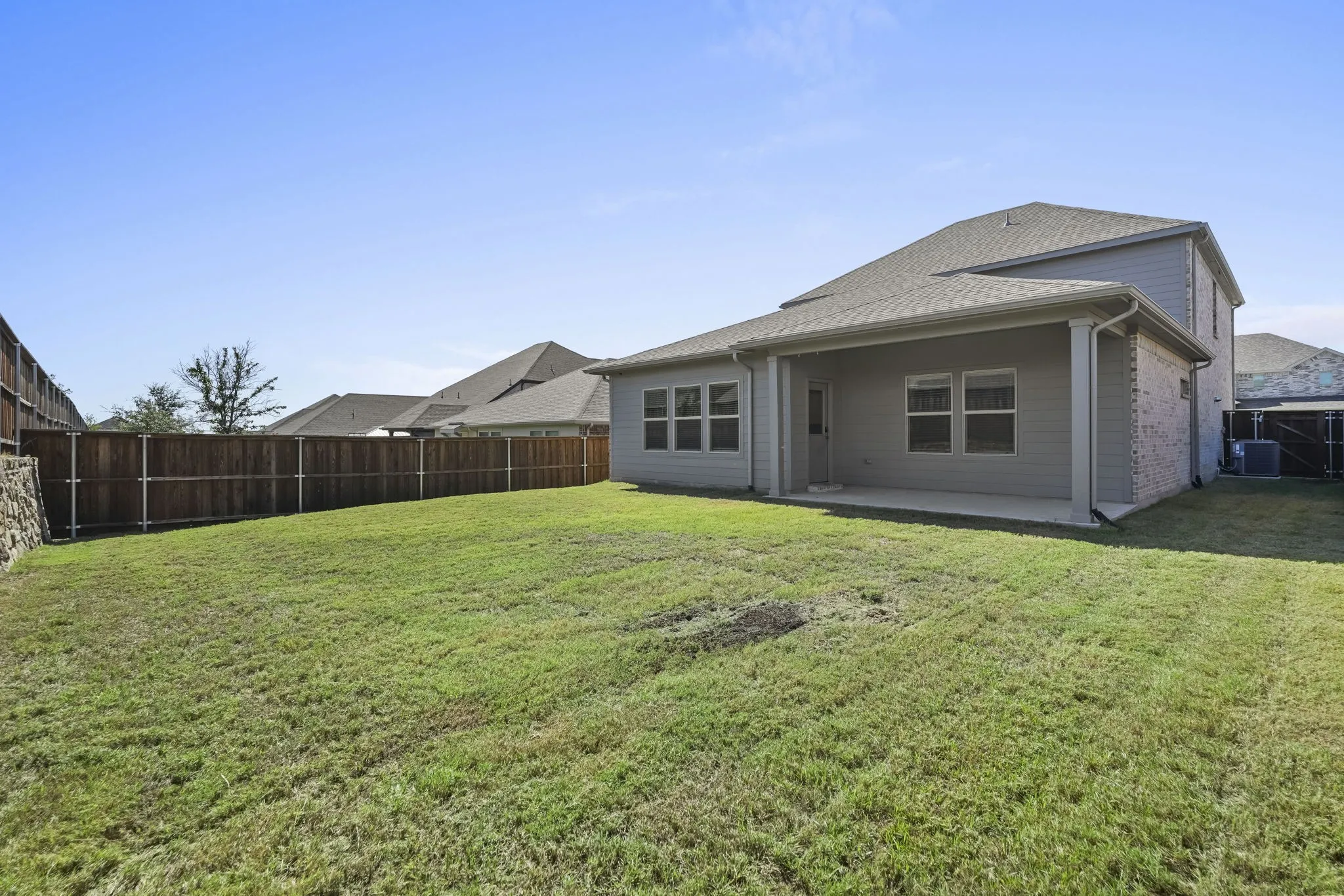 Expansive backyard with a wood privacy fence, concrete patio, and a covered porch