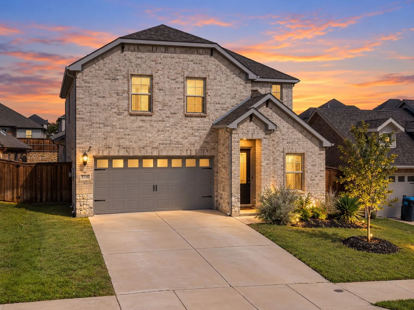 Brick exterior with stone accents, attached two-car garage, concrete driveway, and front yard landscaping