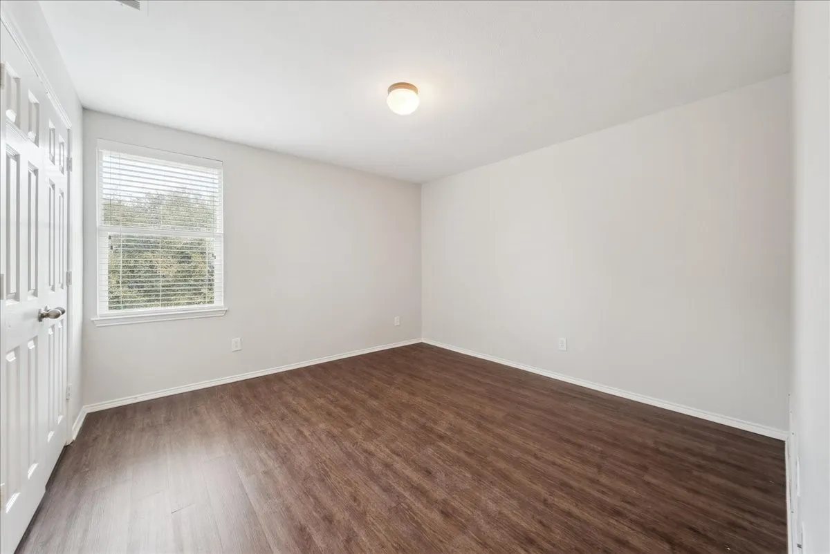 Wood-finish flooring, white painted walls, and a window with horizontal blinds