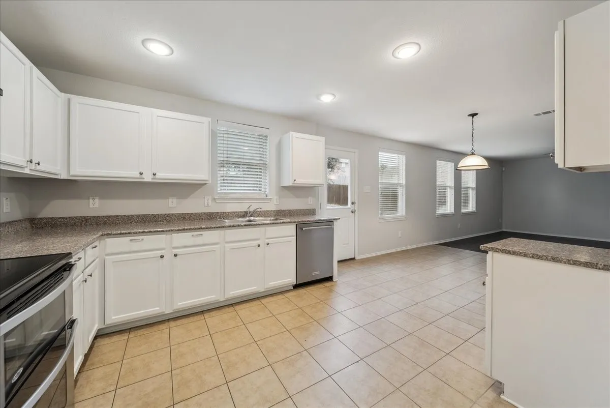 White cabinetry with dark hardware, stone-finish countertops, stainless steel appliances, tile flooring, and recessed lighting