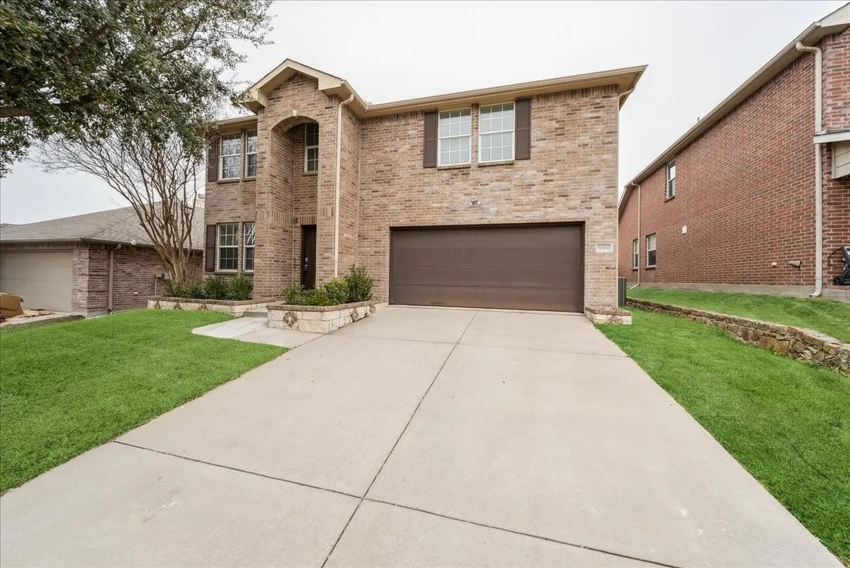 Brick exterior with arched entryway, attached garage, concrete driveway, and stone-edged landscaping beds