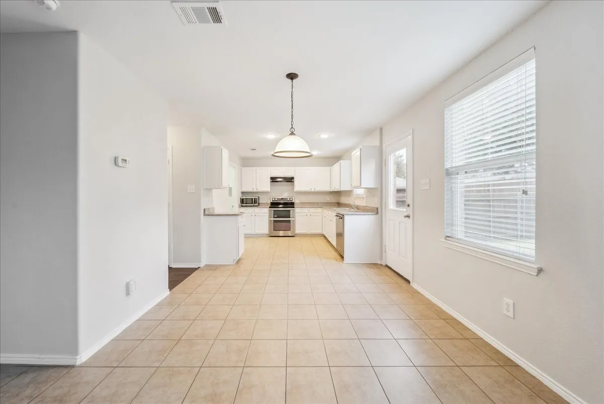Open-concept kitchen and dining area featuring tile flooring, white cabinetry, a pendant light fixture, and stainless steel appliances