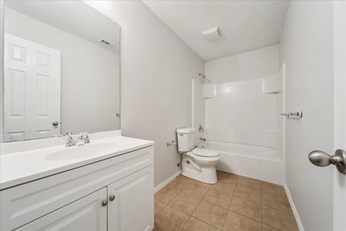Bathroom featuring a white vanity with integrated sink, chrome faucet, wall-mounted mirror, white toilet, and tub-shower combination with white surround