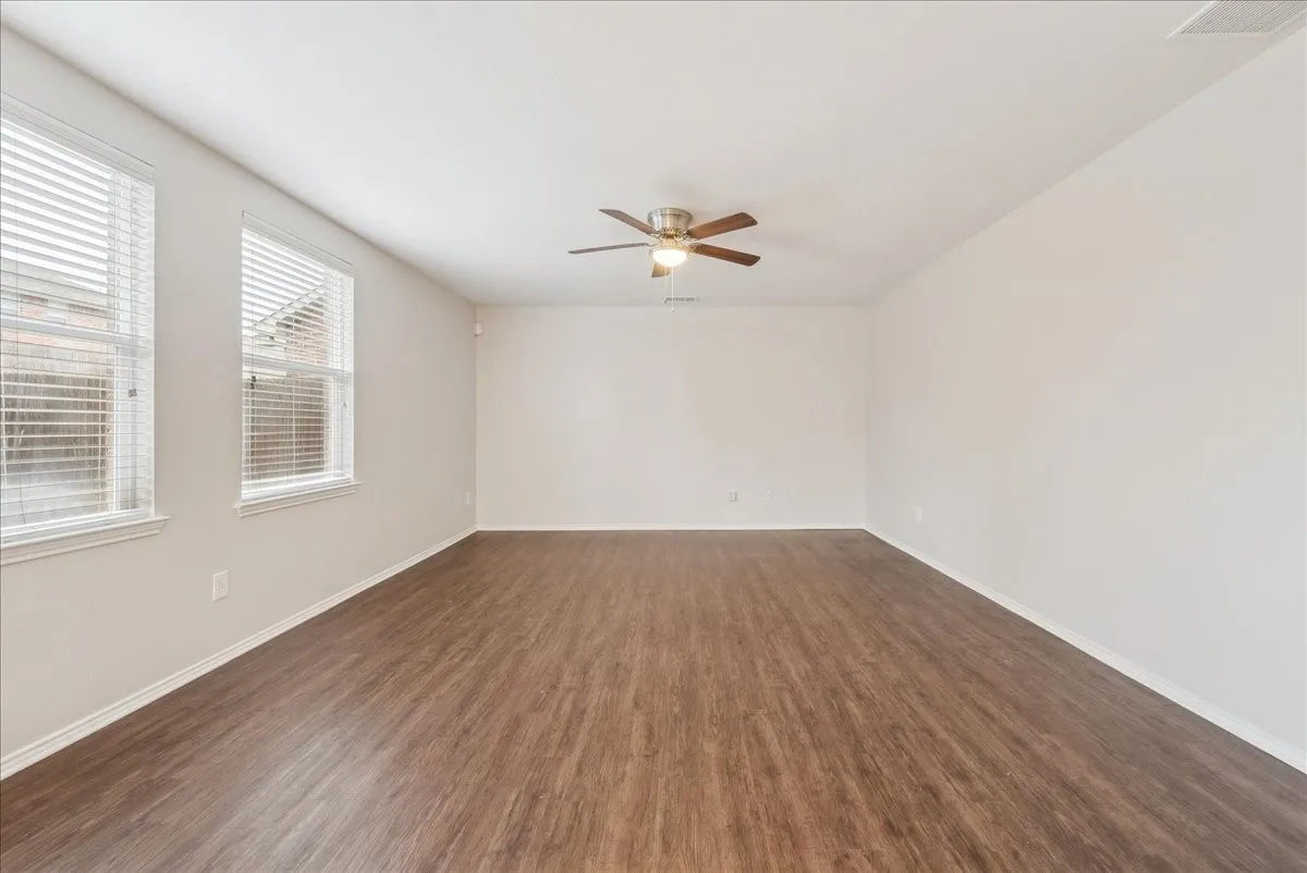 Spacious room featuring wood-finish flooring, multiple windows with blinds, a ceiling fan, and neutral paint
