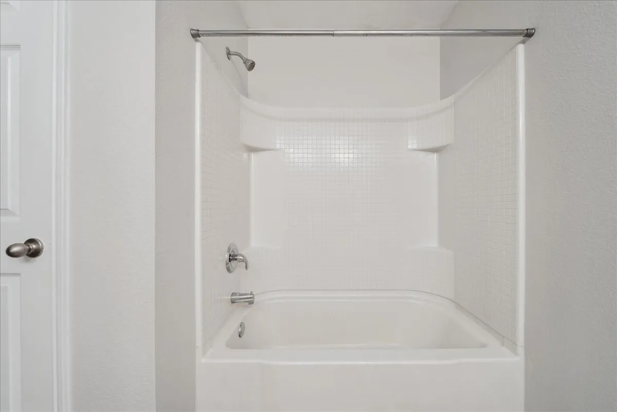 Bathtub with integrated shower surround, chrome showerhead, and coordinating bath faucet