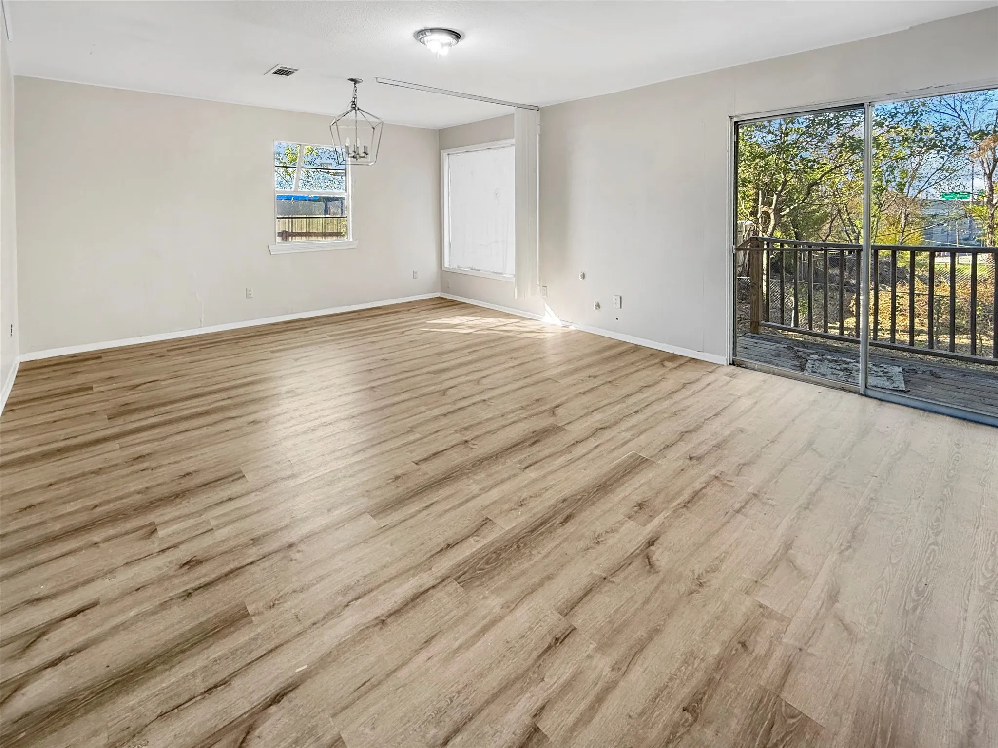 Spacious room featuring wood-finish flooring, a contemporary chandelier, a sliding glass door to an outdoor deck, and a window for natural light