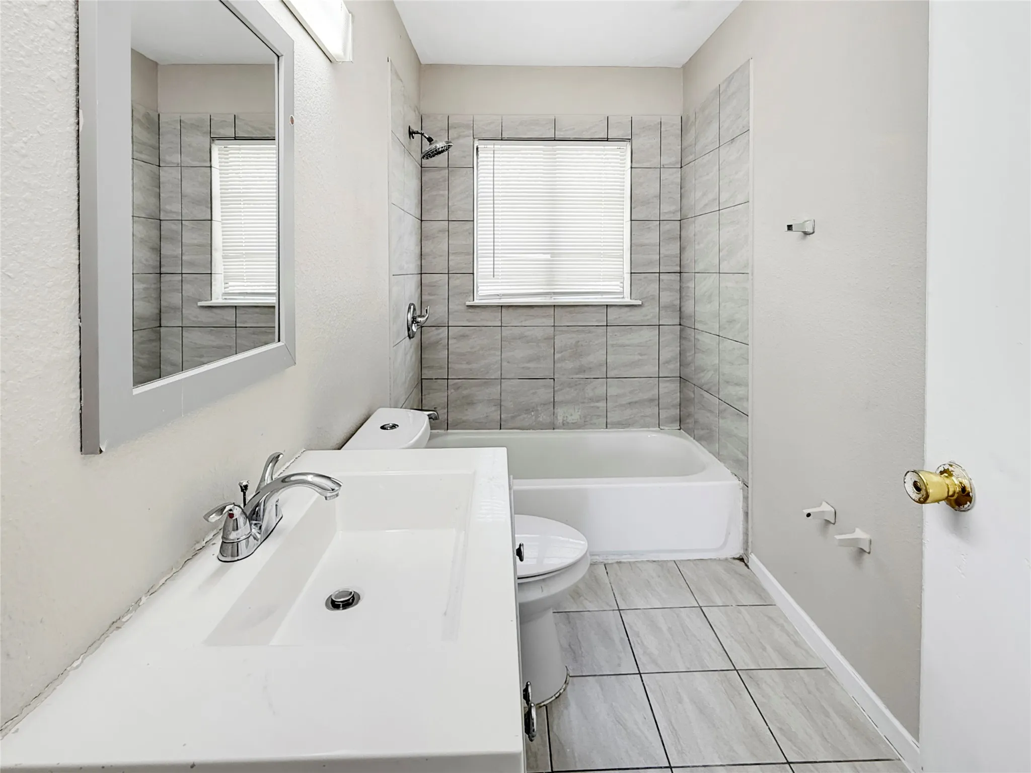 Bathroom featuring a white vanity with integrated sink, chrome faucet, framed mirror, and tiled shower surround with bathtub