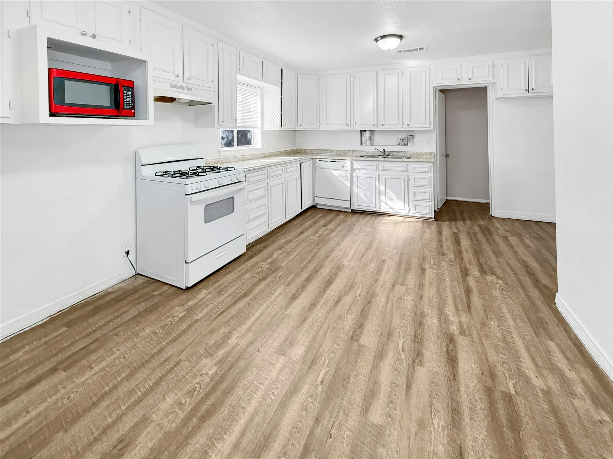 Kitchen with wood-finish flooring, white cabinetry, a built-in oven, and a dishwasher