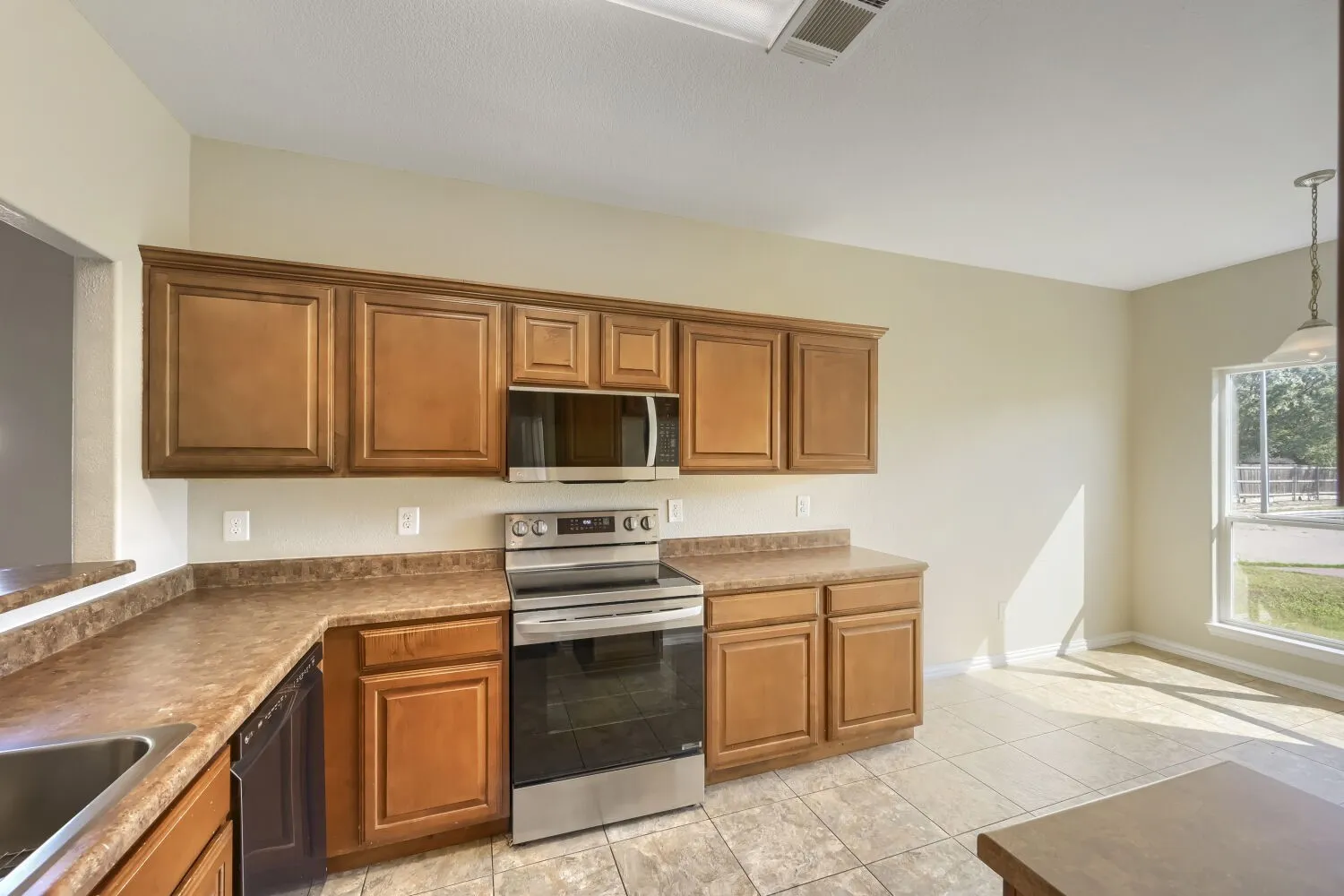 Wood-finish cabinetry with crown molding, stainless steel range and microwave, and tile flooring