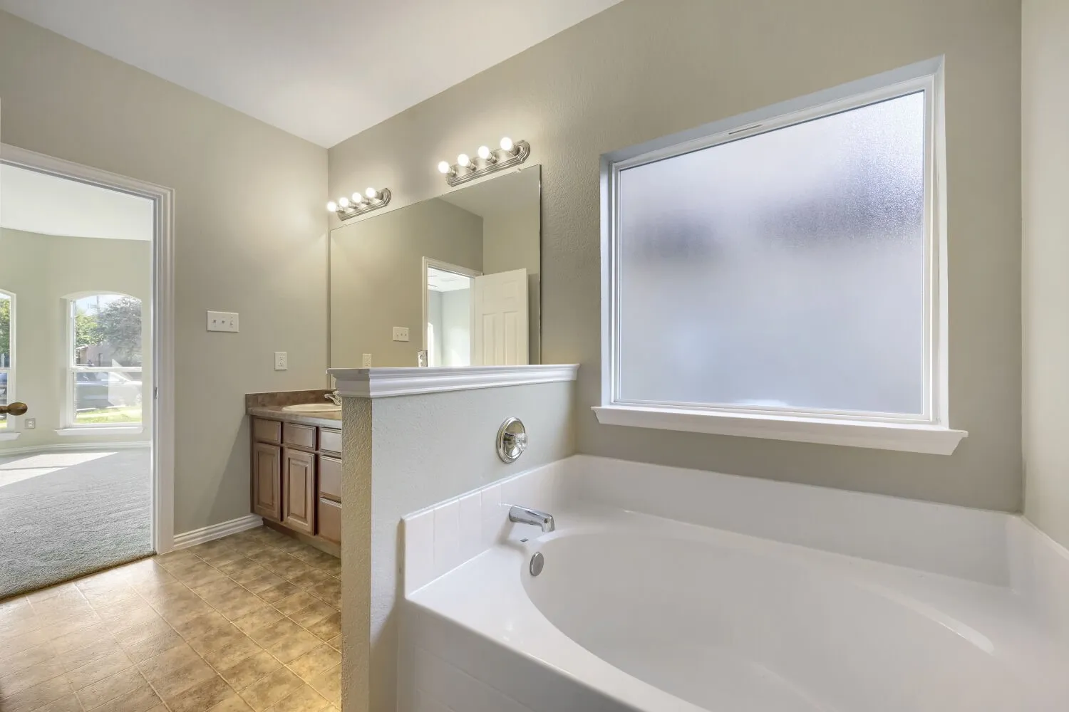 Built-in soaking tub with chrome fixtures, frosted privacy window, and tile flooring