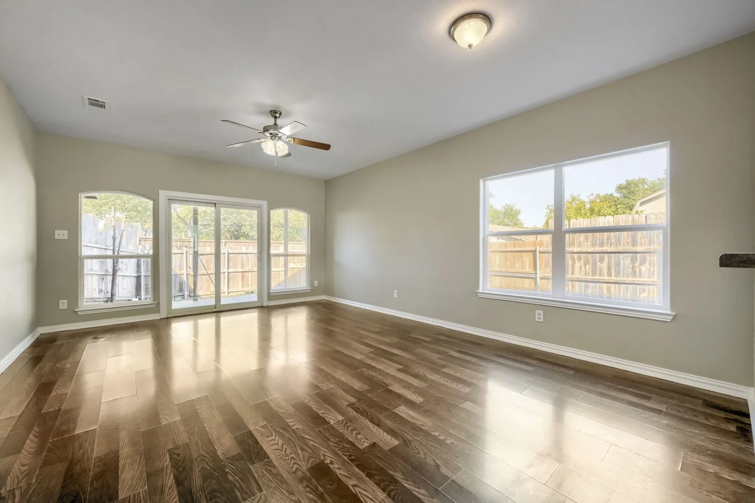 Rich wood-finish flooring, sliding glass patio doors, multiple large windows, and a ceiling fan with integrated lighting
