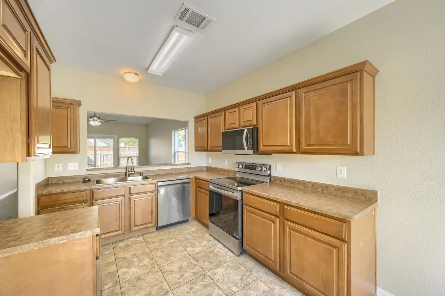 Kitchen featuring wood-finish cabinetry, stainless steel appliances, a dual basin sink, and tile flooring