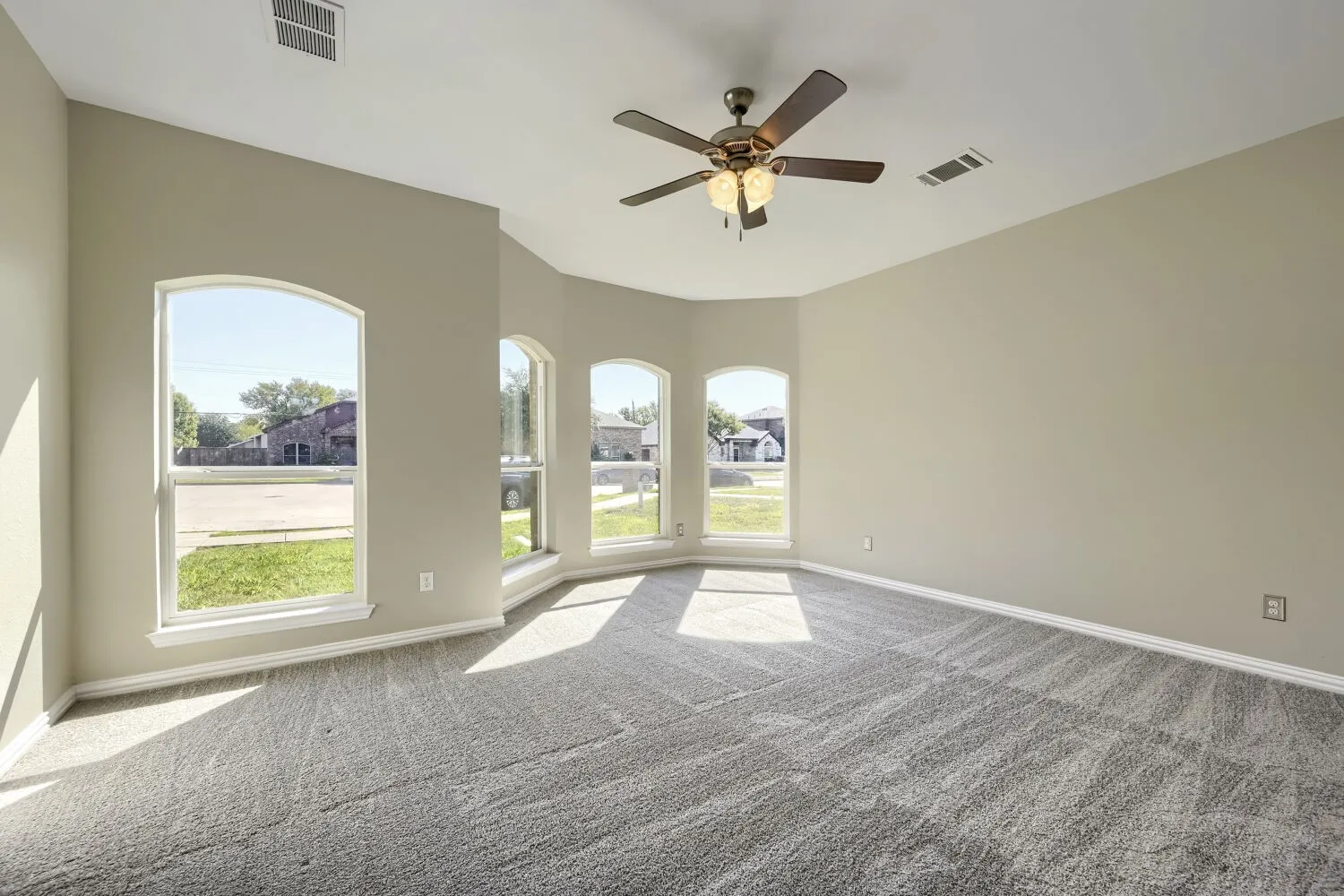 Arched windows, recessed ceiling, ceiling fan with integrated lighting, and neutral-toned carpet