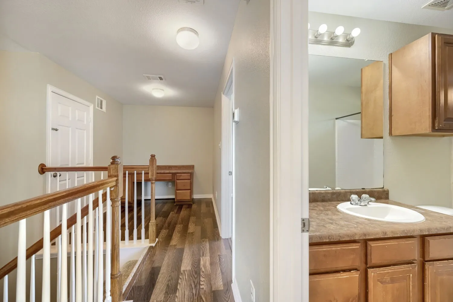 Wood-finish flooring throughout, white baluster staircase with wood handrail, and built-in desk