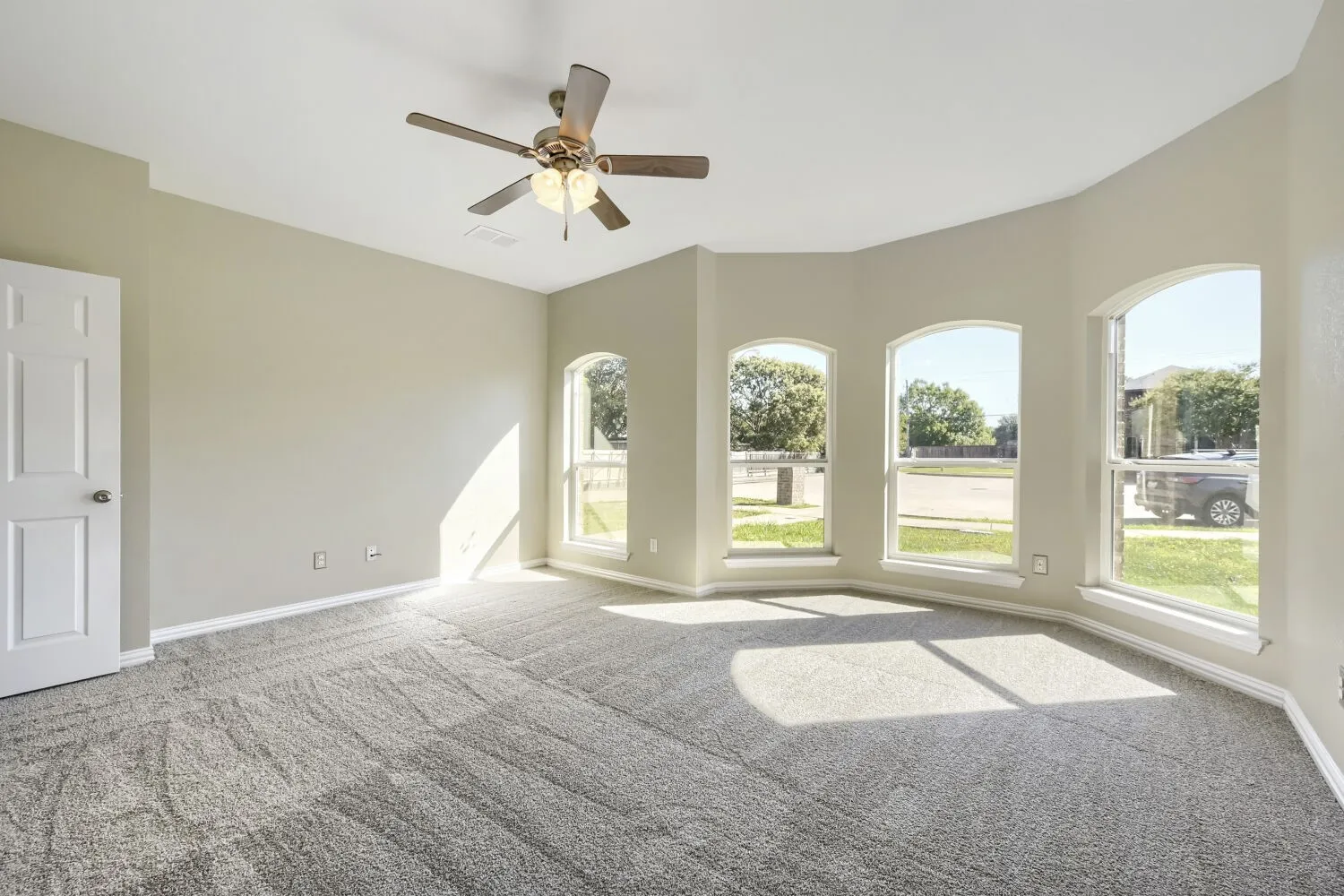 Recessed ceiling with a ceiling fan, arched windows, light-toned walls, and grey carpeting