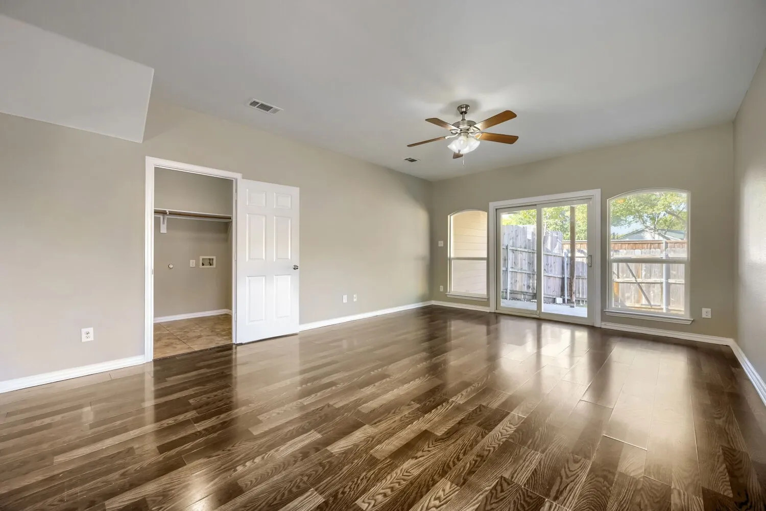 Wood-finish flooring, vaulted ceiling, ceiling fan, sliding glass door, and arched windows