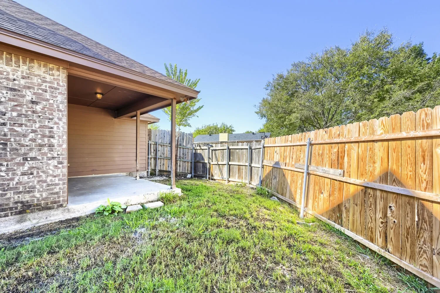 Covered patio with concrete flooring, brick exterior, and wood fencing