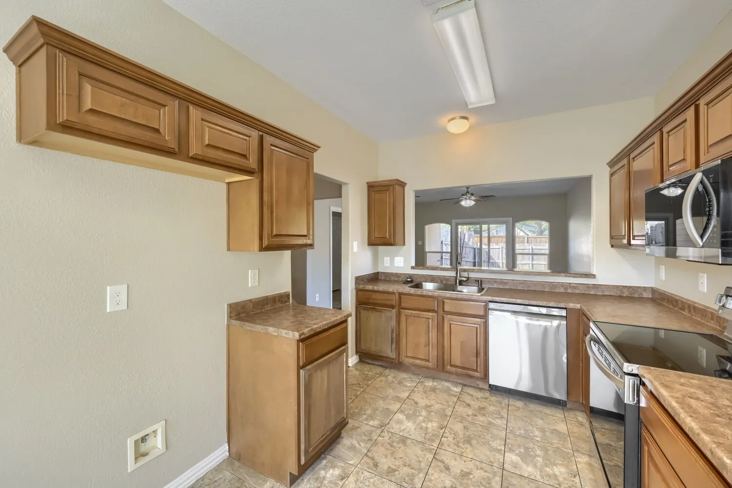 Kitchen featuring wood cabinetry, laminate countertops, a stainless steel dishwasher, a built-in microwave, and tile flooring