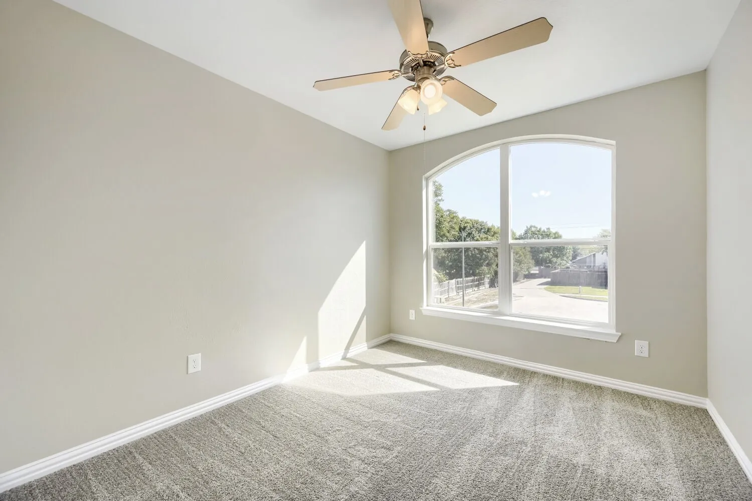 Vaulted ceiling with a ceiling fan, arched window, and textured carpet flooring