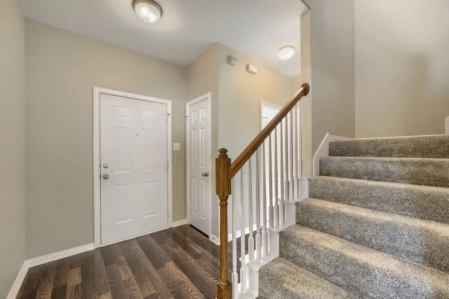 Entryway with wood-finish flooring, two panel doors, and a carpeted staircase featuring a wood handrail with white balusters