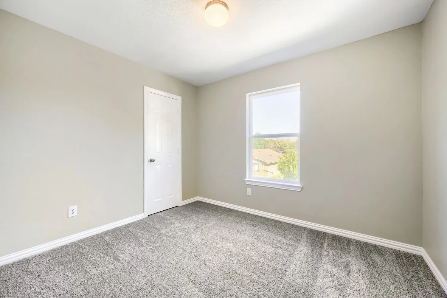 Neutral tone wall paint, textured carpeting, single window with roller shade, white trim, and a ceiling-mounted light fixture