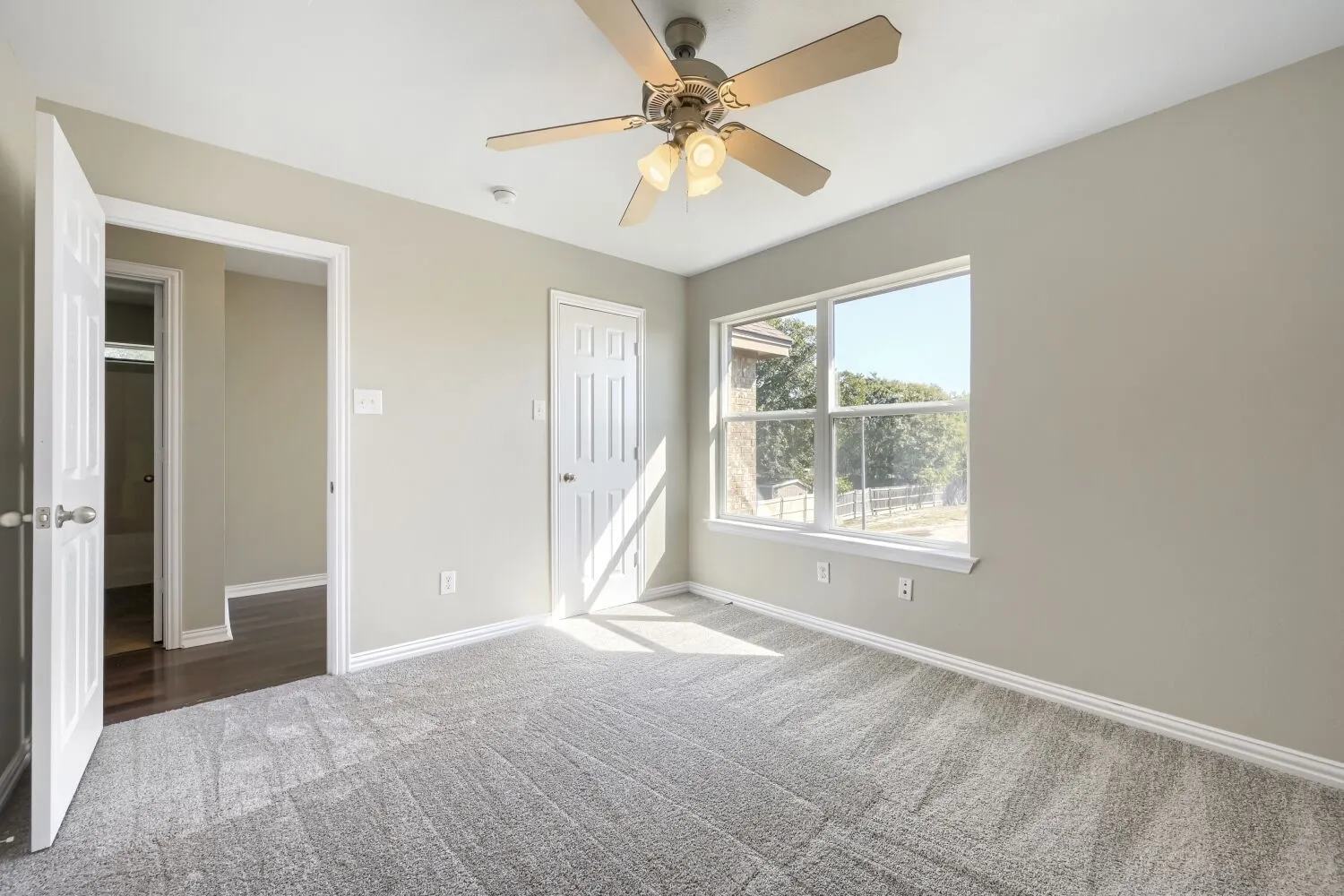 Neutral-toned walls, gray carpeting, and a ceiling fan with integrated lighting