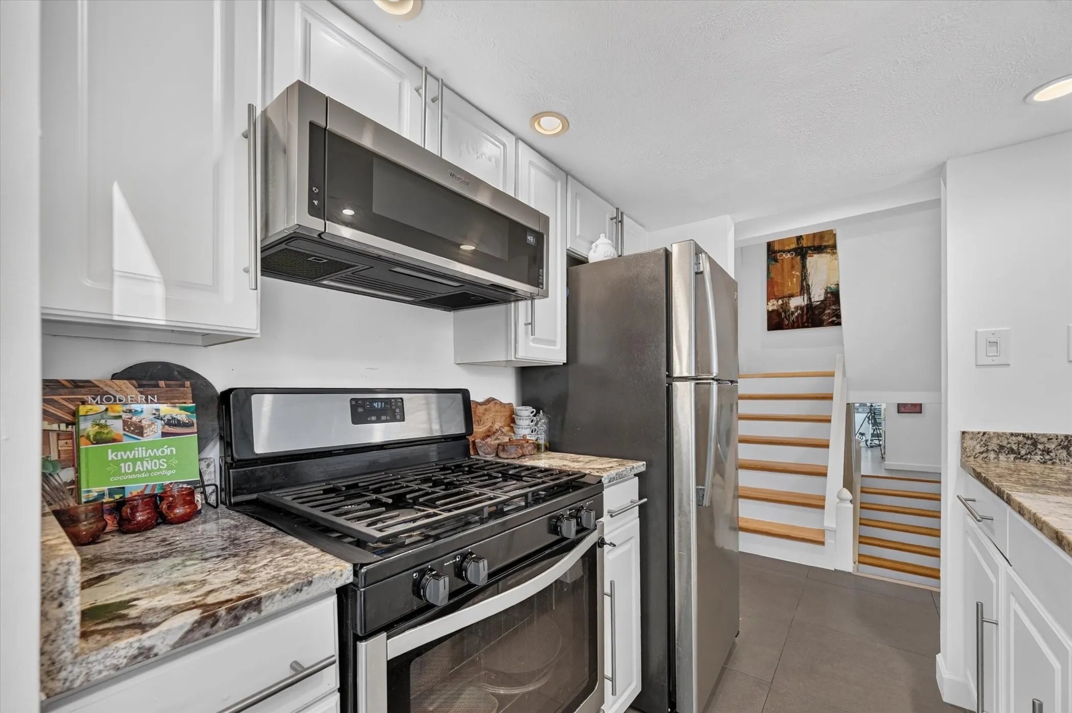 Stainless steel appliances, white cabinetry, recessed lighting, stone countertops, and a built-in microwave