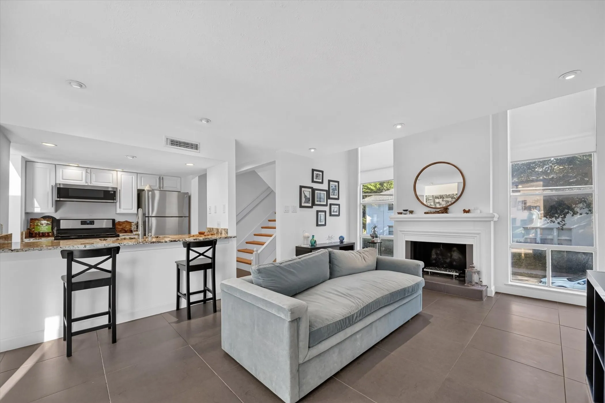 Open-concept living area with tiled flooring, a fireplace featuring a classic white mantel, and large windows