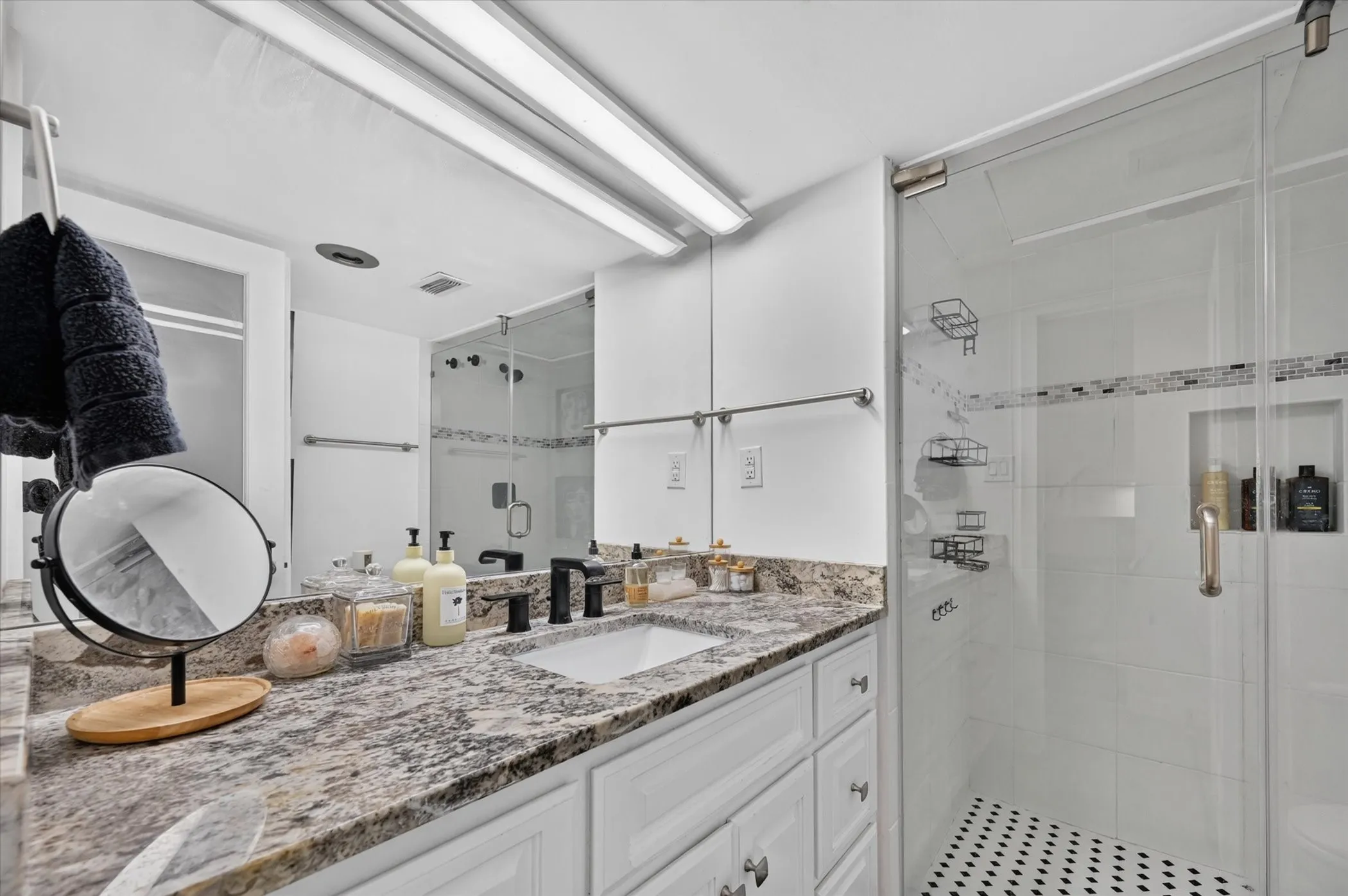 White vanity with integrated sink, granite-style countertop, matte black faucet, and glass-enclosed shower with mosaic tile accent
