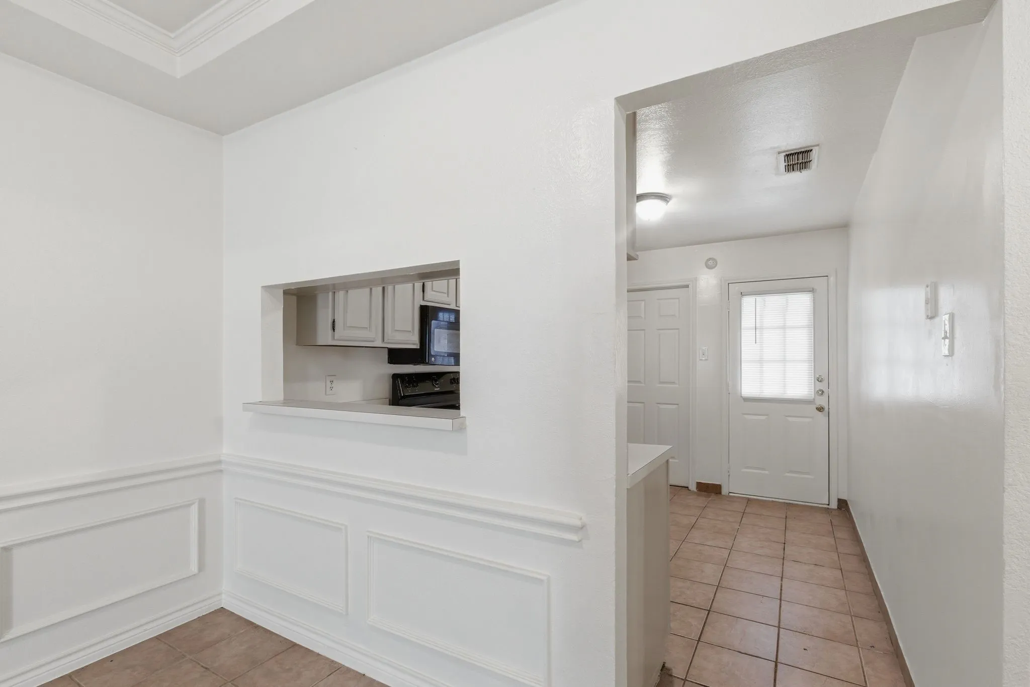 Pass-through window with counter, built-in wall paneling, crown molding, and tiled flooring