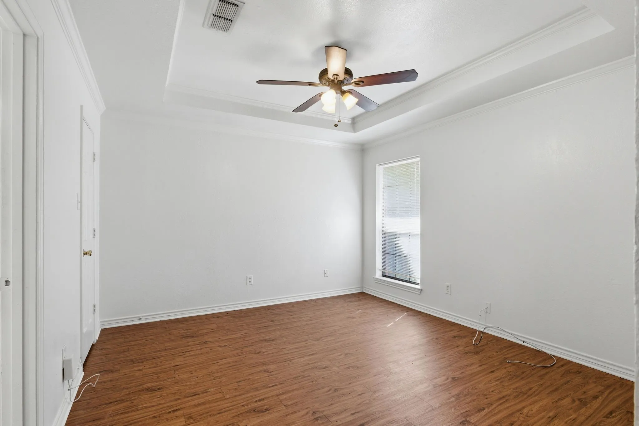 Tray ceiling with crown molding, wood-finish flooring, ceiling fan with light kit, and a single window with blinds