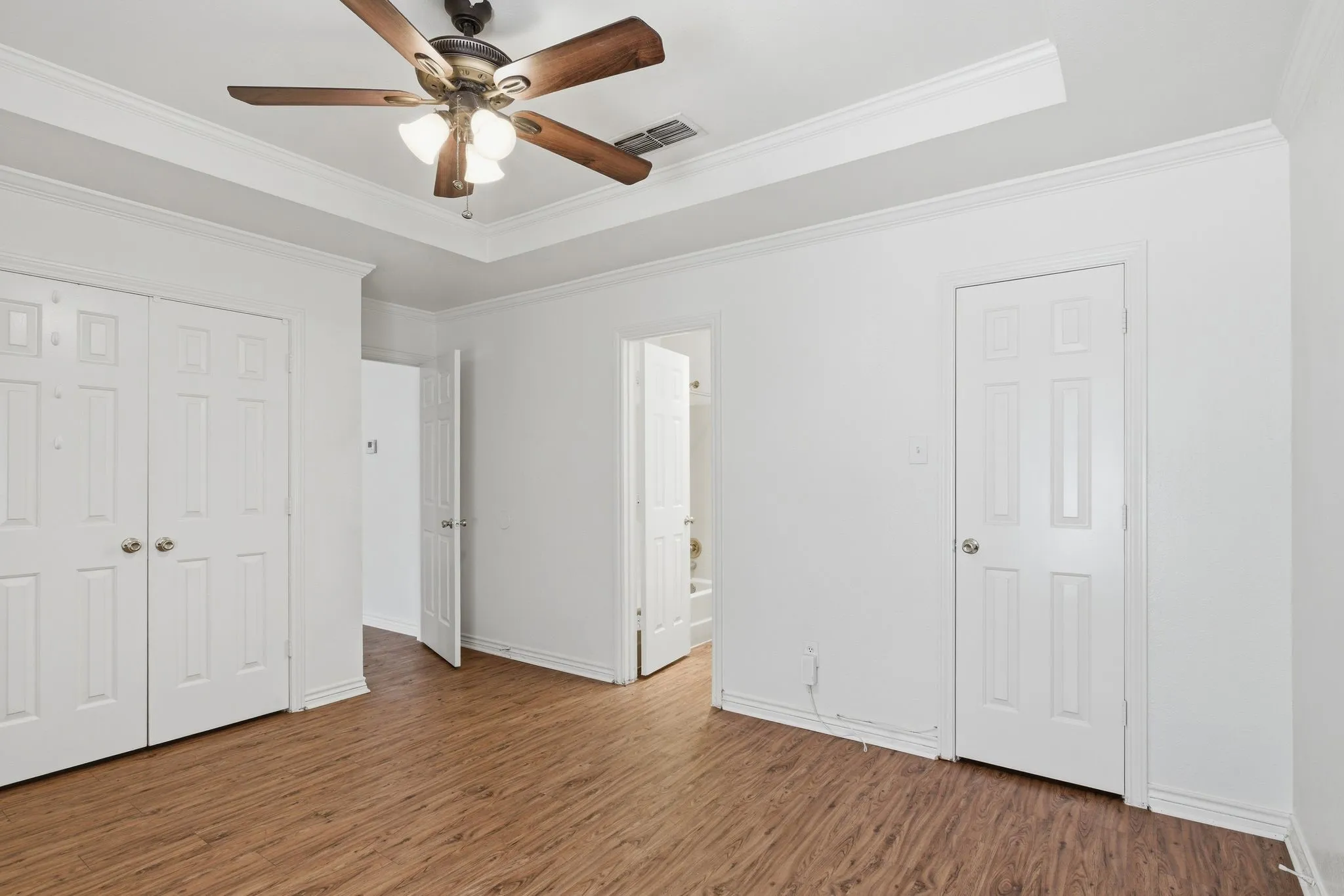 Tray ceiling with crown molding and a ceiling fan, wood-finish flooring, and white paneled doors