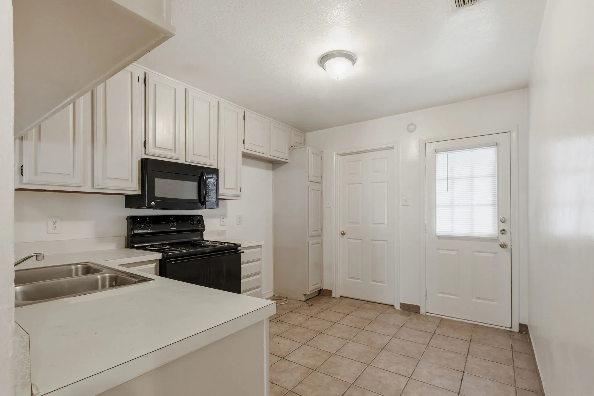 White cabinetry, dual basin stainless steel sink, black electric range, black microwave, and tile flooring