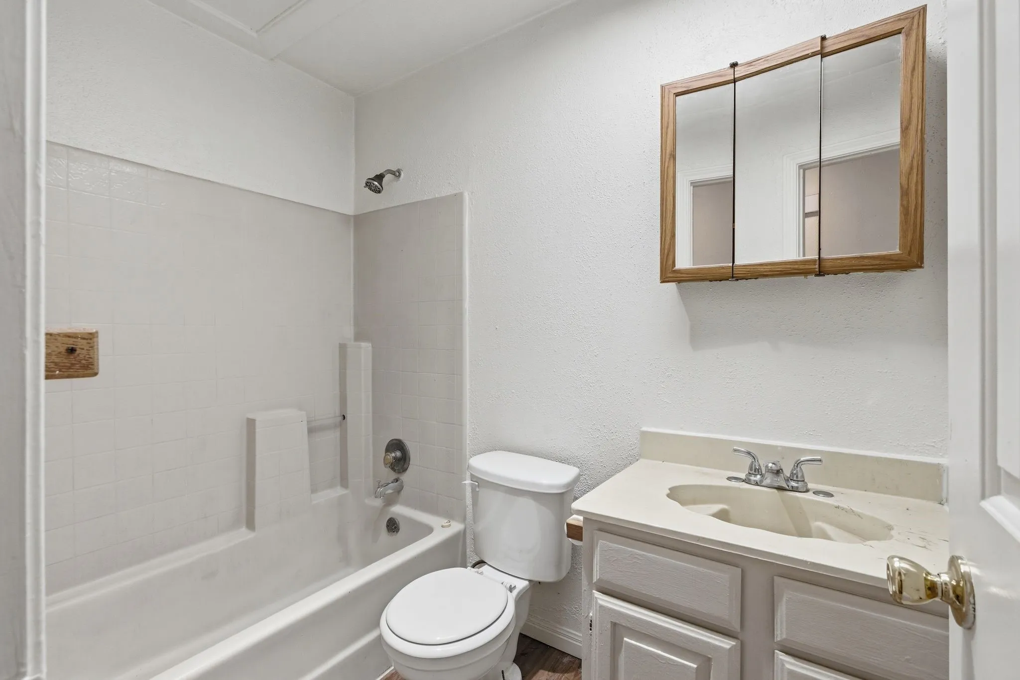 Bathroom featuring a white bathtub with tile surround, a toilet, a vanity with a light-colored countertop, and a wood-framed medicine cabinet