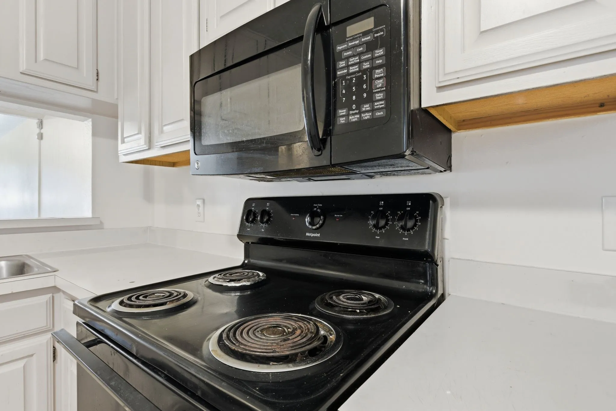 White paneled cabinetry, white countertops, black oven, and black microwave