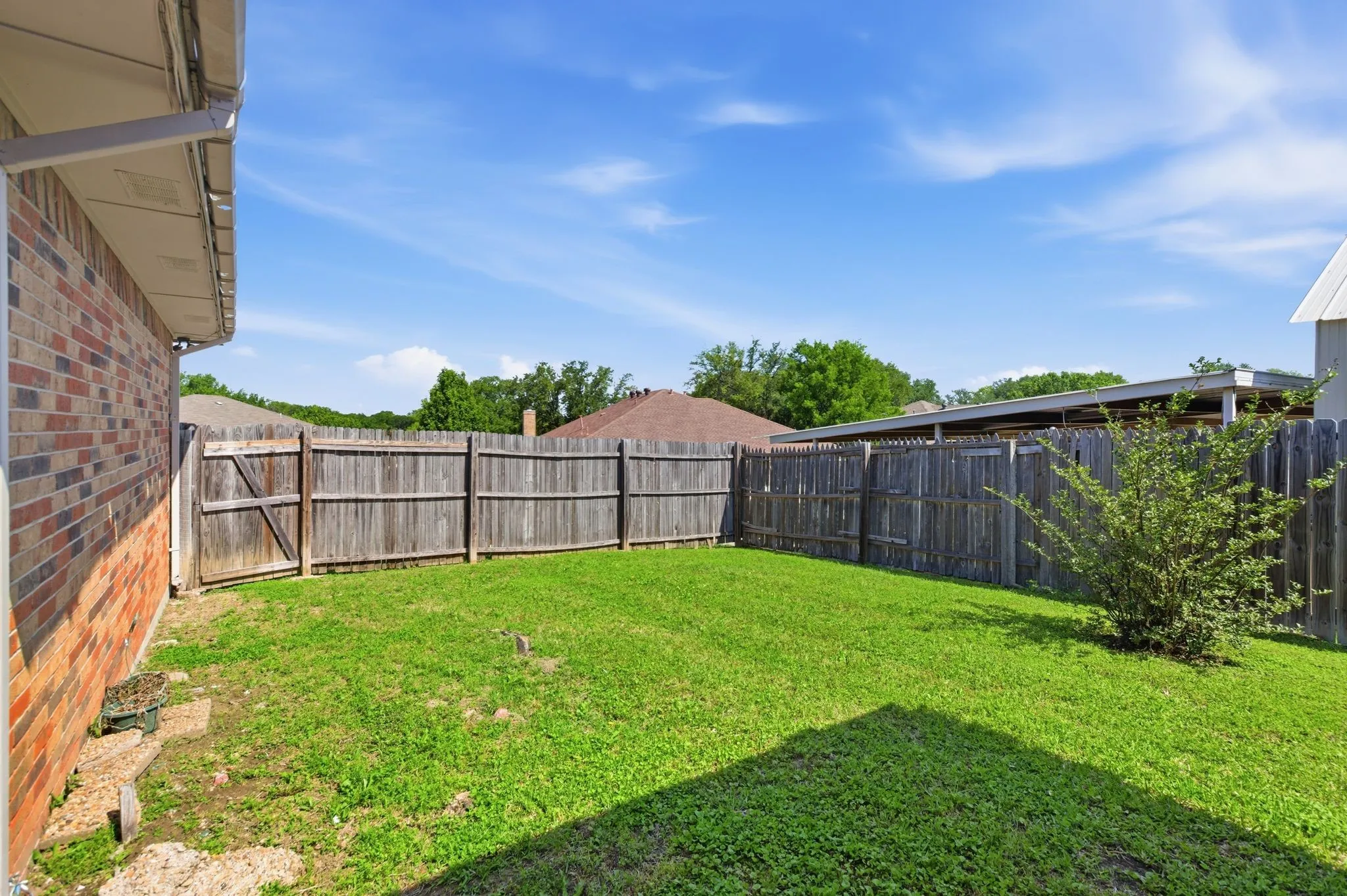 Enclosed backyard featuring a privacy fence, established shrubbery, and a brick exterior