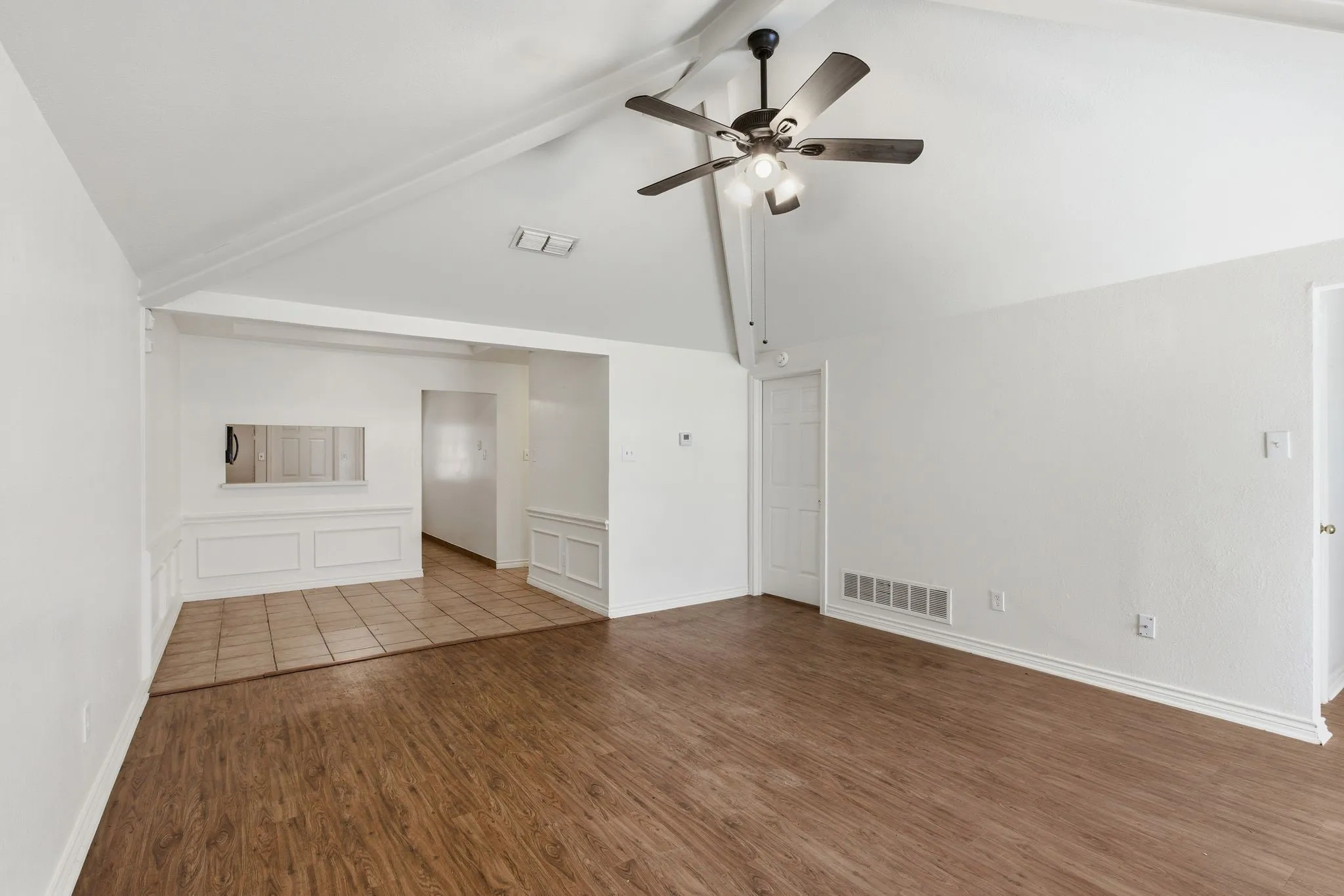 Vaulted ceilings with exposed beams, wood-finish flooring, tile flooring, ceiling fan with integrated lighting, and wainscoting