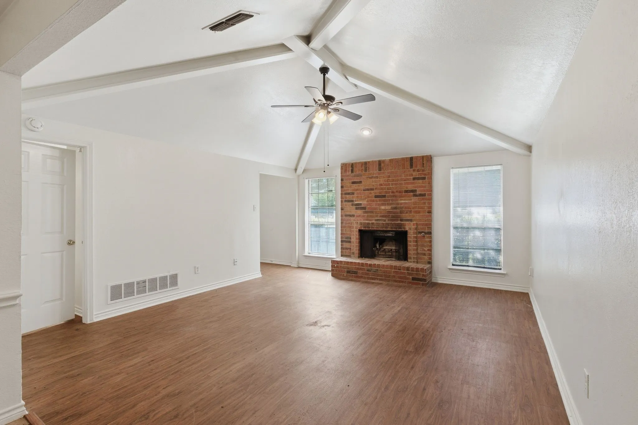 Vaulted ceiling with exposed beams, wood-finish flooring, brick fireplace, ceiling fan, and recessed lighting