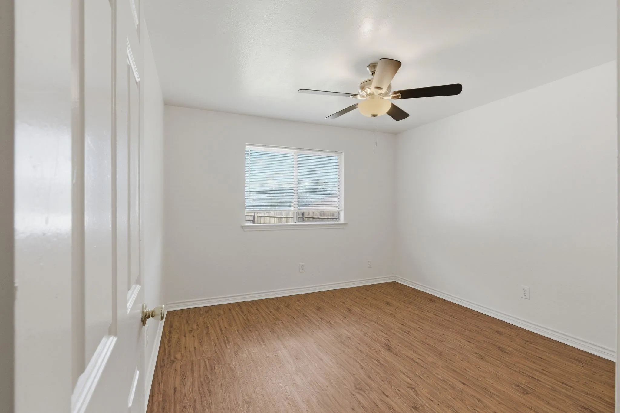 Wood-finish flooring, white walls, and a ceiling fan with integrated lighting