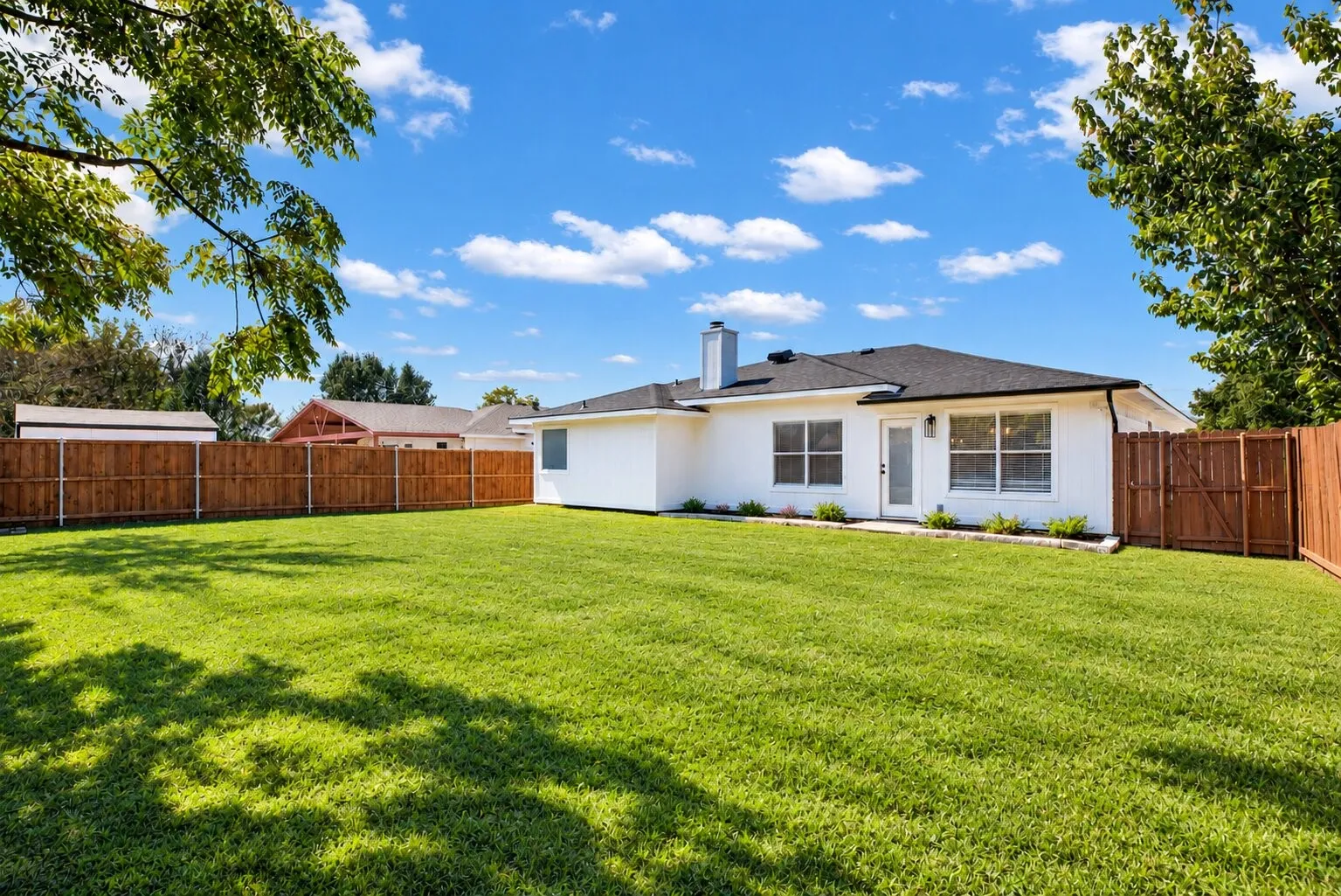 Expansive backyard with a manicured lawn, complete wood privacy fencing, and a crisp white exterior