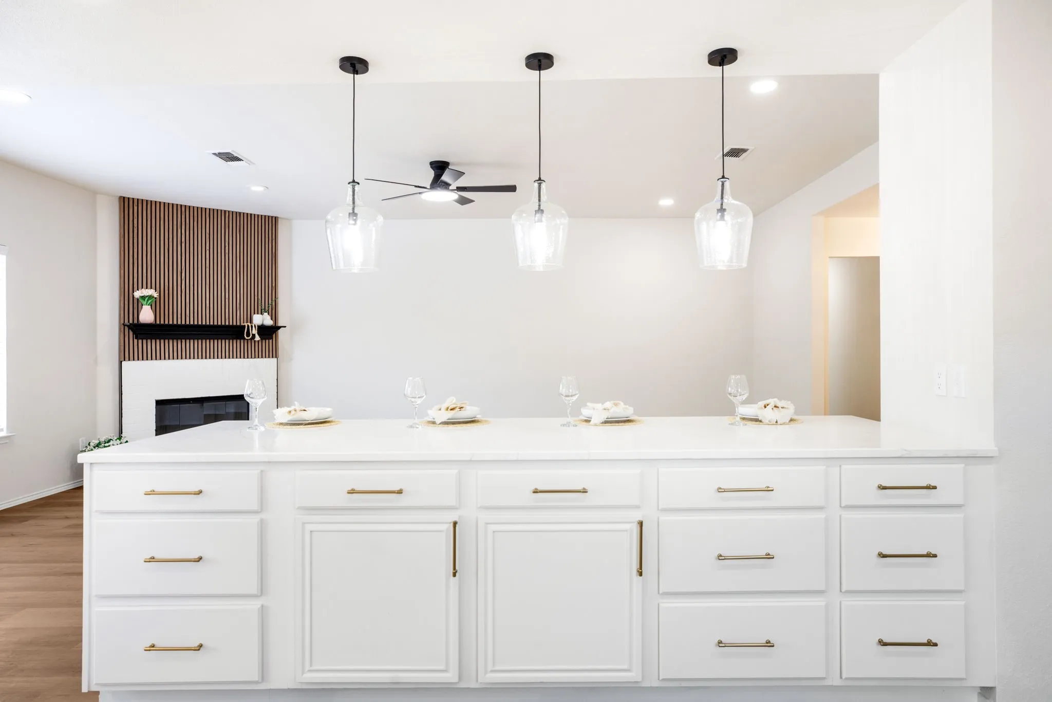 White kitchen island with gold-finish hardware, three pendant lights, and recessed ceiling lights