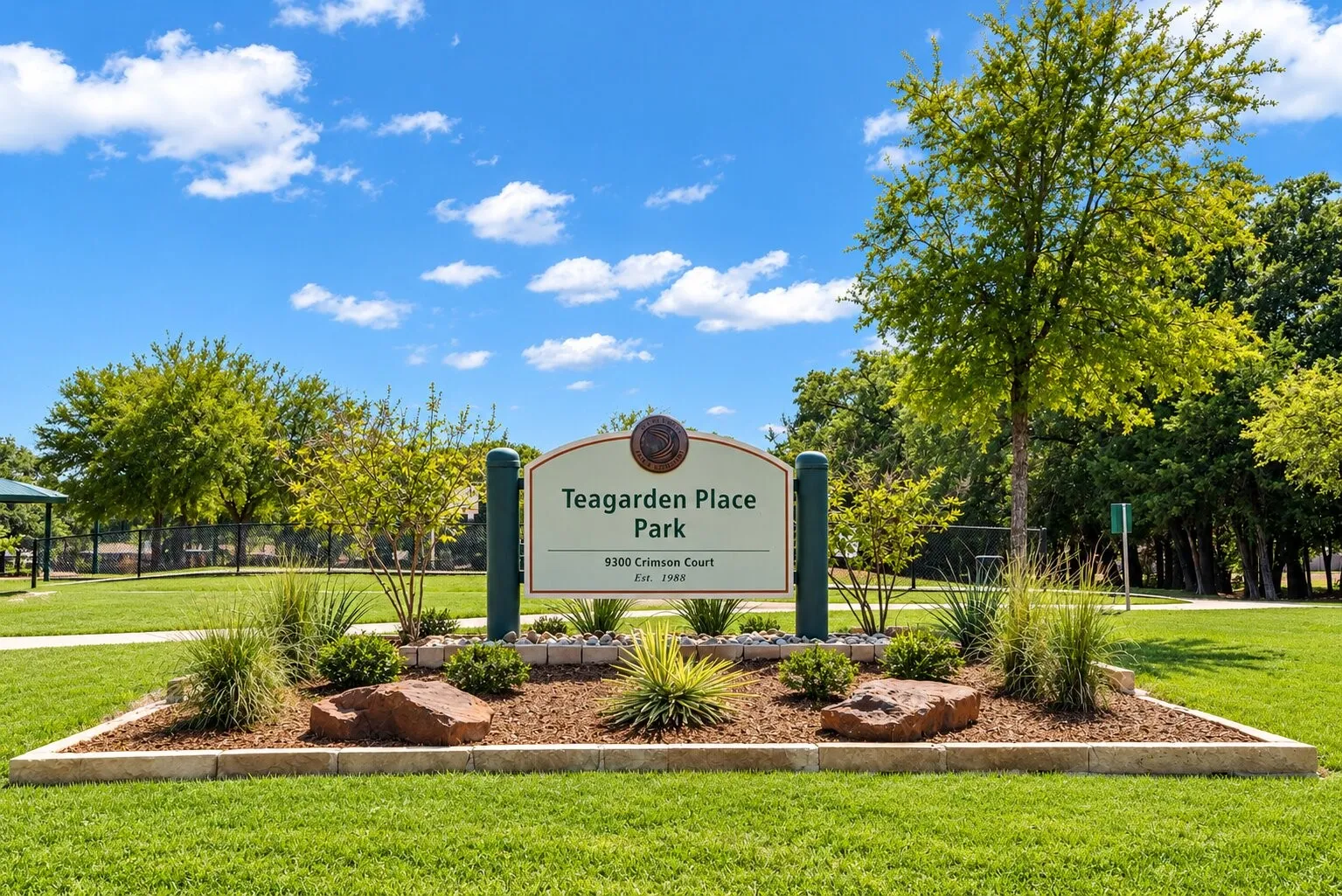 Teagarden Place Park sign with a landscaped base, set against a backdrop of mature trees and green space