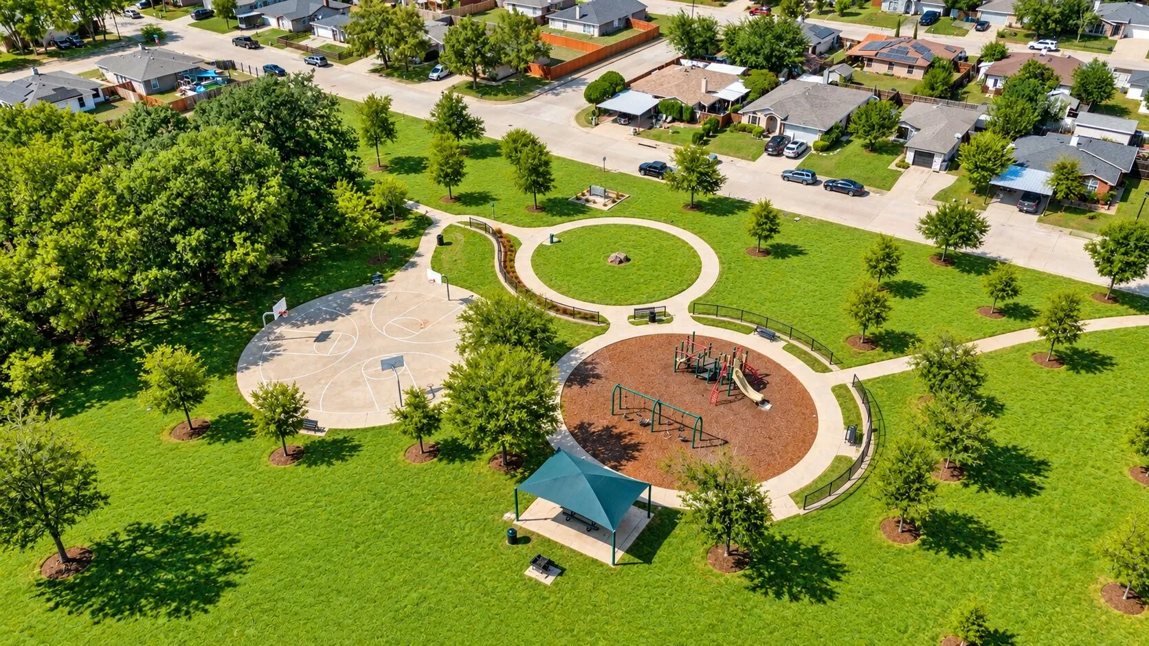 Expansive green space featuring walking paths, a dedicated playground area, basketball court, and mature trees